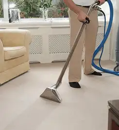 Professional carpet cleaner using a hot-water extraction wand and hose machine in a living room in Charlotte, NC.