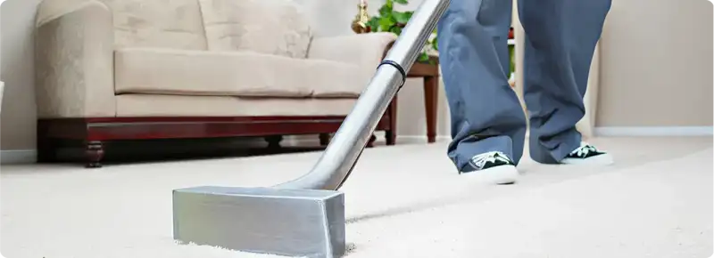 Carpet cleaning technician using a hot-water extraction wand on a light-colored carpet in a living room, Charlotte, NC.