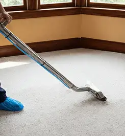 Steam carpet cleaning technician using a hot-water extraction wand on a residential carpet, wearing blue protective shoe covers Charlotte, NC.