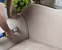 Professional upholstery cleaner deep-cleaning a fabric sofa with a handheld extraction tool and hose in Charlotte, NC.